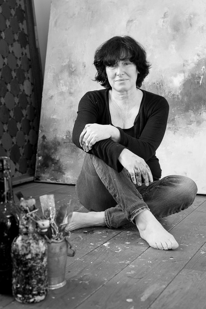 Kitty van de Rijt seated on the studio floor in front of an unfinished canvas, paint on her hands.